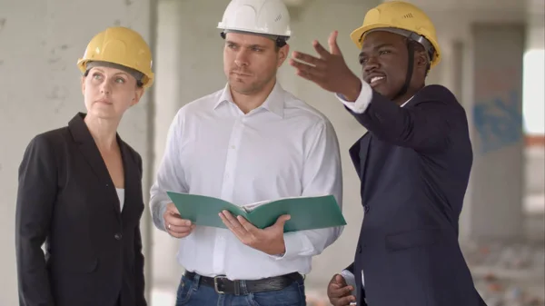 Grupo de construtores sorridentes em hardhats com prancheta e planta ao ar livre — Fotografia de Stock