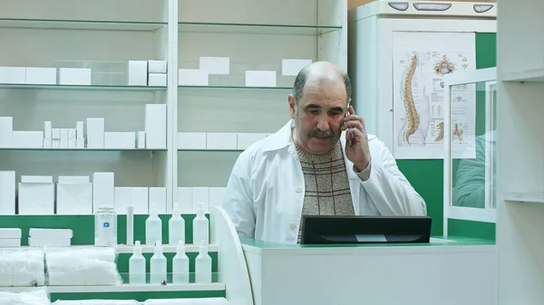 Фармацевт розмовляє з клієнтом за допомогою мобільного телефону в аптеці Ліцензійні Стокові Фото