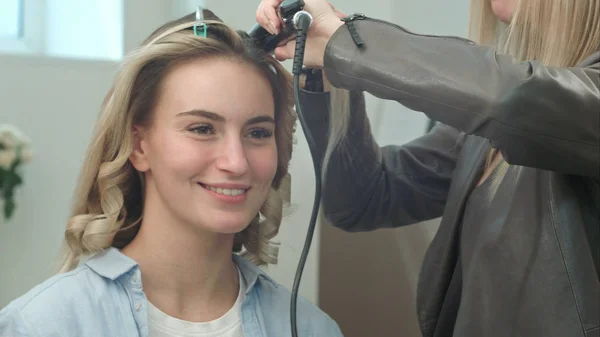 Професійний перукар використовує волосся прямолінійного випрямлення волосся, розмовляючи з клієнтом — стокове фото