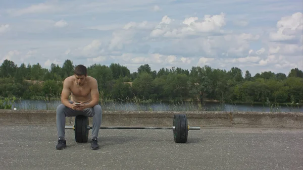 Deportista masculino usando su teléfono móvil mientras toma un descanso después de un intenso entrenamiento activo al aire libre — Foto de Stock