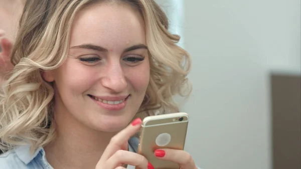 Mujer peinado de pelo en el salón mientras navega por Internet en su teléfono móvil, sonriendo — Foto de Stock