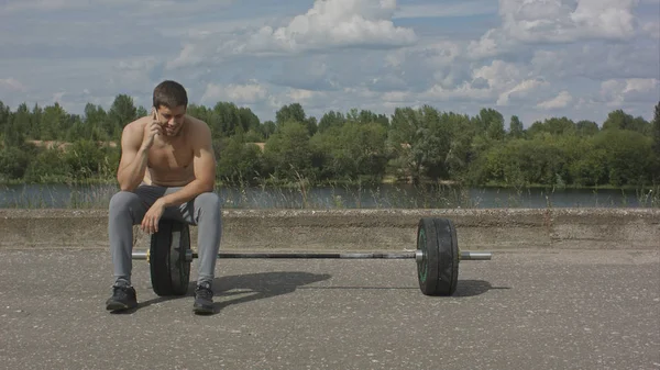 Athletic bearded man with muscular body having phone call after training outdoor