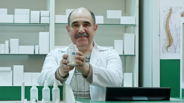 Усміхнений лікар тримає пляшку таблеток, радячи клієнтам, які дивляться на камеру — стокове фото