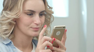 Mutlu genç sarışın bir kadın güzellik salonunda oturan ve bir smartphone kullanarak