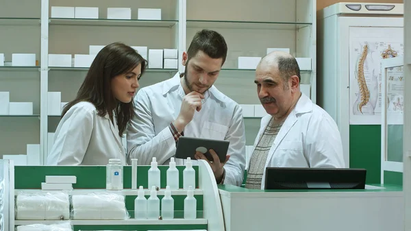 Três farmacêuticos concentrados usando tablet em um balcão em uma farmácia — Fotografia de Stock
