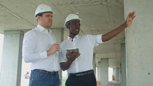 Ledningsgruppen på byggarbetsplats granska med tablett formella klädda människor som läser konstruktion tablett framför byggnaden — Stockfoto