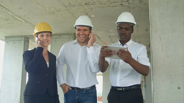 Equipe executiva em canteiro de obras discutindo projeto, usando tablet, tendo ligações telefônicas com smartphone — Fotografia de Stock
