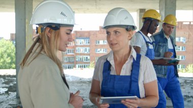 Female engineer and worker on construction site with plan on digital tablet clipart