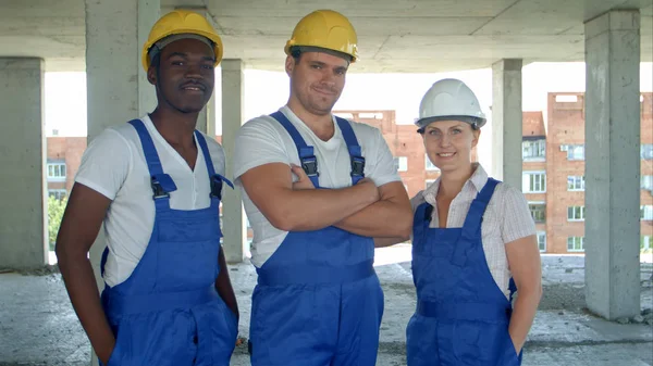 Equipe diversa confiante de trabalhadores e mulheres de pé agrupados em suas masmorras e chapéus duros sorrindo para a câmera — Fotografia de Stock