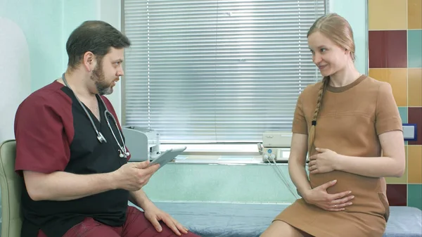 Доктор розмовляє з вагітною жінкою і дивиться на цифровий планшет — стокове фото