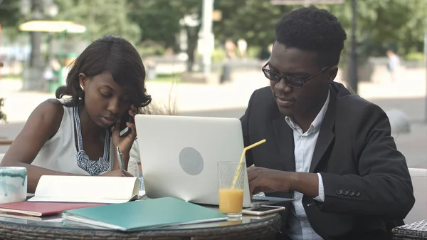 Un collègue africain et une collègue travaillant ensemble, utilisant des gadgets lors d'une réunion dans un café — Photo