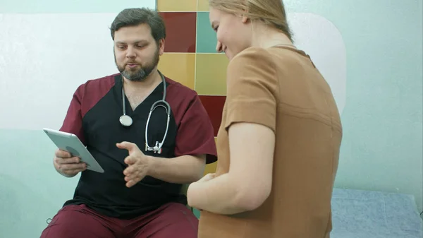 Лікар і вагітна жінка дивляться на цифровий планшет разом — стокове фото