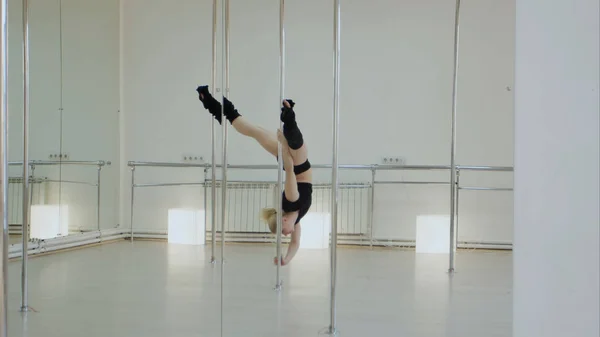 Невероятный танцор с шестом делает раскол, пока висит вверх ногами на пилоне в студии — стоковое фото