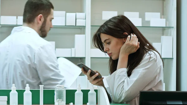 Une pharmacienne ennuyée utilise son téléphone portable à la pharmacie — Photo