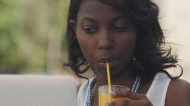Dizüstü bilgisayar kullanarak ve suyu içme kafede masada oturan boş vaktinizi rahat kıyafetler içinde güzel afro Amerikan kadın