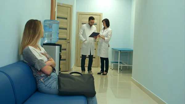 Ανησυχούν γυναίκα ασθενής περιμένει στην αίθουσα νοσοκομείου ενώ δύο γιατρούς που συζητάμε για διάγνωση — Φωτογραφία Αρχείου