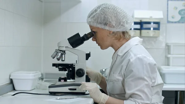 Jolie chercheuse médicale écrivant des notes tout en utilisant son microscope dans un laboratoire — Photo