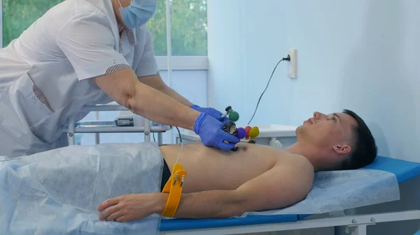 Медсестра прикрепляет электроды к груди пациентов мужского пола — стоковое фото
