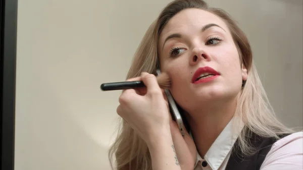 Mooie jongedame toepassing van make-up op het gezicht met borstel, na telefoontje, te laat — Stockfoto