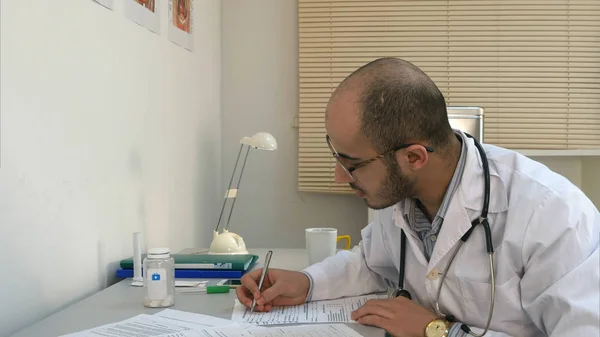 Απασχολημένος αρσενικό ιατρό εργασίας με έγγραφα και έχοντας τηλεφωνική συνομιλία στο γραφείο του — Φωτογραφία Αρχείου
