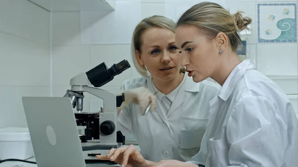 Two young laboratory technician with laptop and a microscope in the laboratory