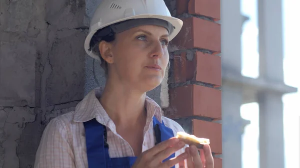 Uma trabalhadora de construção come um sanduíche em um canteiro de obras — Fotografia de Stock