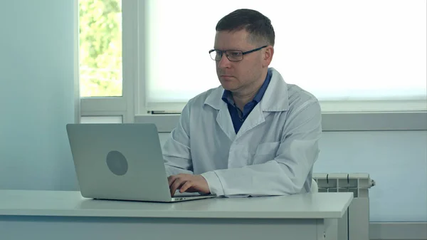 Чоловік лікар працює на портативному комп'ютері на білому столі в лікарні — стокове фото