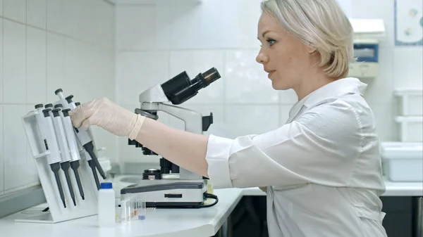 Jeune femme travaillant avec des liquides et un microscope — Photo