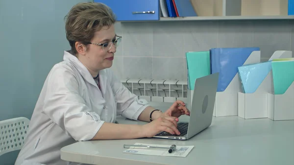 Концентрированная женщина-врач в очках, печатающая на ноутбуке в офисе — стоковое фото