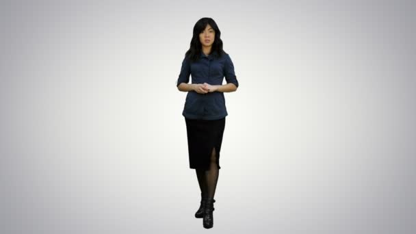 Молода приваблива азіатка розмовляє з камерою, представляючи щось на білому тлі — стокове відео