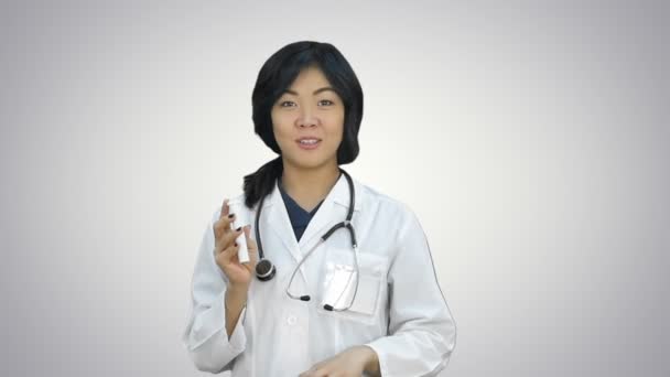 Asiatico medico femminile che mostra una bottiglia di compresse, presentando pillole su sfondo bianco — Video Stock