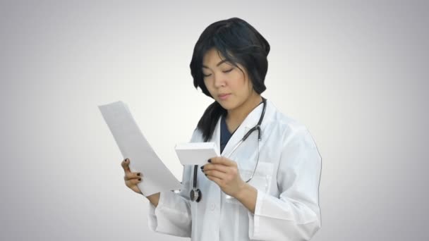 Asiático feminino médico leitura prescrição e olhando para caixa de medicina no fundo branco — Vídeo de Stock