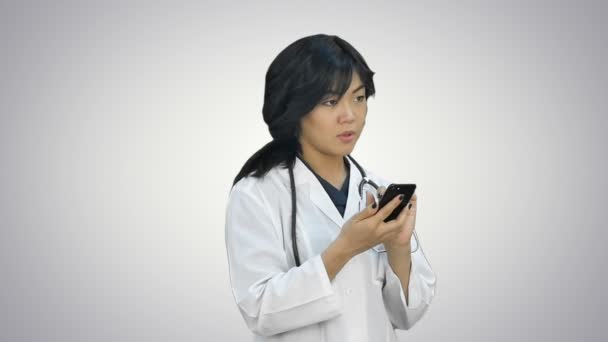 Pensivo asiático mulher médico usando telefone inteligente no fundo branco — Vídeo de Stock