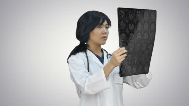 Mujer asiática médico usando un blanco abrigo y estetoscopio mirando x ray en blanco fondo — Vídeos de Stock