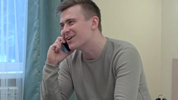 Hombre joven y saludable sonriendo y hablando por teléfono inteligente en casa — Foto de Stock