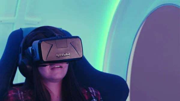 Chica sorprendida experimentando la realidad virtual en una silla interactiva en movimiento —  Fotos de Stock