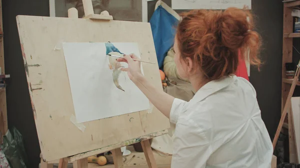 Young female artist painting still life in studio