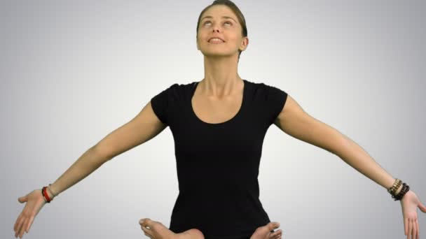 Молода жінка, сидячи в лотосі йога позує практикуючи медитацію на білому тлі — стокове відео