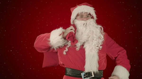 Real Papai Noel carregando presentes em seu saco em fundo vermelho com neve — Fotografia de Stock