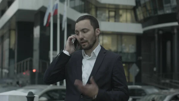 Hombre de negocios ruso contestando la llamada por teléfono y explicar algo a los socios de negocios, de pie fuera de la oficina — Foto de Stock