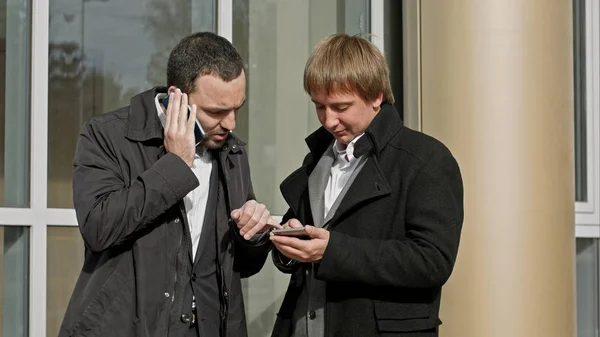 Two businessmen talking on mobile phone and reading message