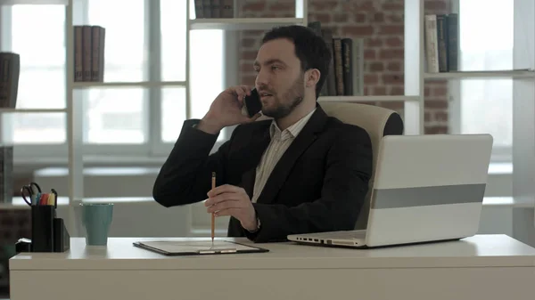Чоловік розмовляє на мобільному телефоні, використовуючи ноутбук — стокове фото