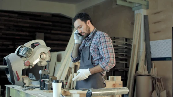Carpenter working on his craft in a dusty workshop and speak phone.