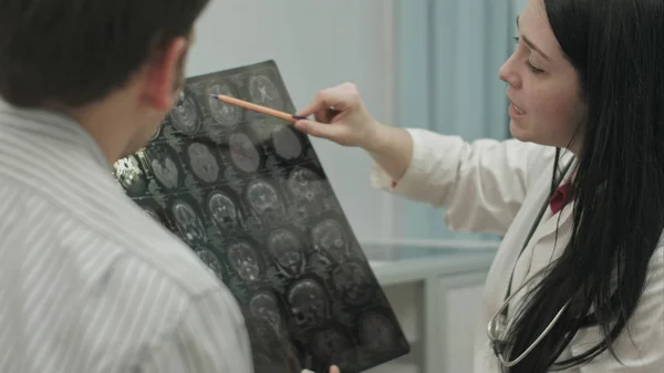 Médico femenino en clínica muestra radiografías a paciente masculino . — Foto de Stock