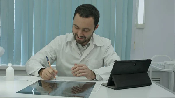 Glücklicher männlicher Arzt, der im Büro arbeitet, schreibt, lächelt. — Stockfoto