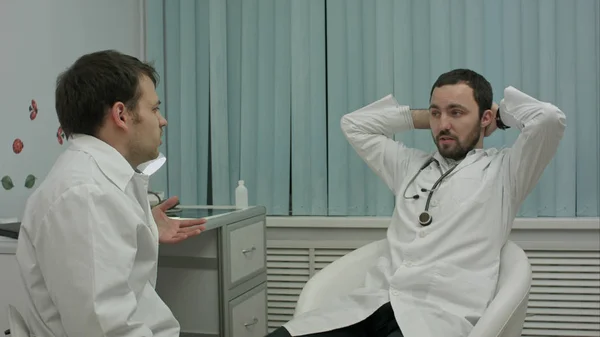 Dwóch lekarzy relaksujący w nowoczesny szpital pomieszczeniu, mówiąc o życiu i pracy — Zdjęcie stockowe