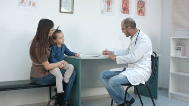 Onların sorunu açıklayan küçük kızıyla anne sırasında tıbbi formu doldurarak çocuk doktoru