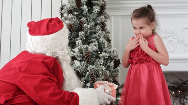 Santa Claus giving present to a surprised little girl and hugging her