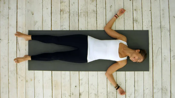 Attraente giovane donna che si allena a casa, facendo esercizio di yoga, sdraiata nel cadavere di Shavasana o nella posizione del corpo morto, riposandosi dopo la pratica, meditando, respirando — Foto Stock