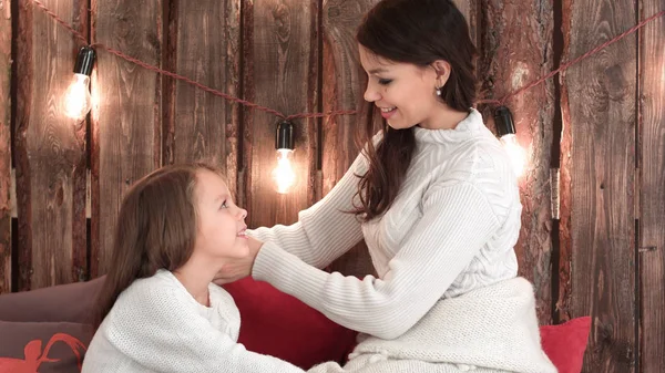 Young mother in white sweater plaiting her daughter hair